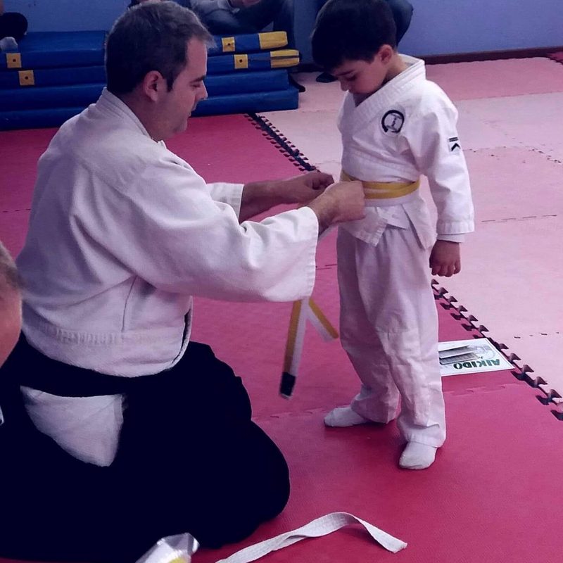 El maestro anudando el cinturón a un alumno infantil
